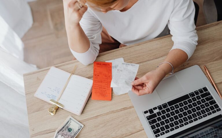 Vrouw bekijkt bonnetjes en haar financiën achter een laptop