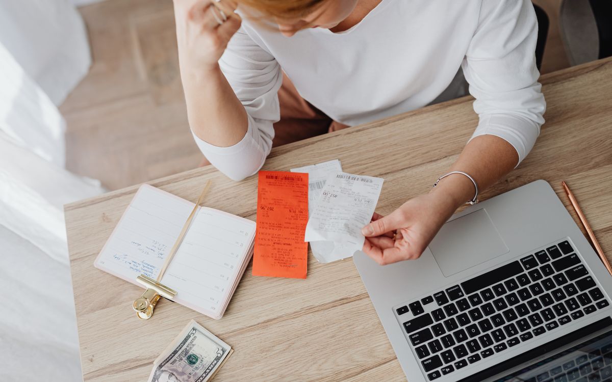 Vrouw bekijkt bonnetjes en haar financiën achter een laptop